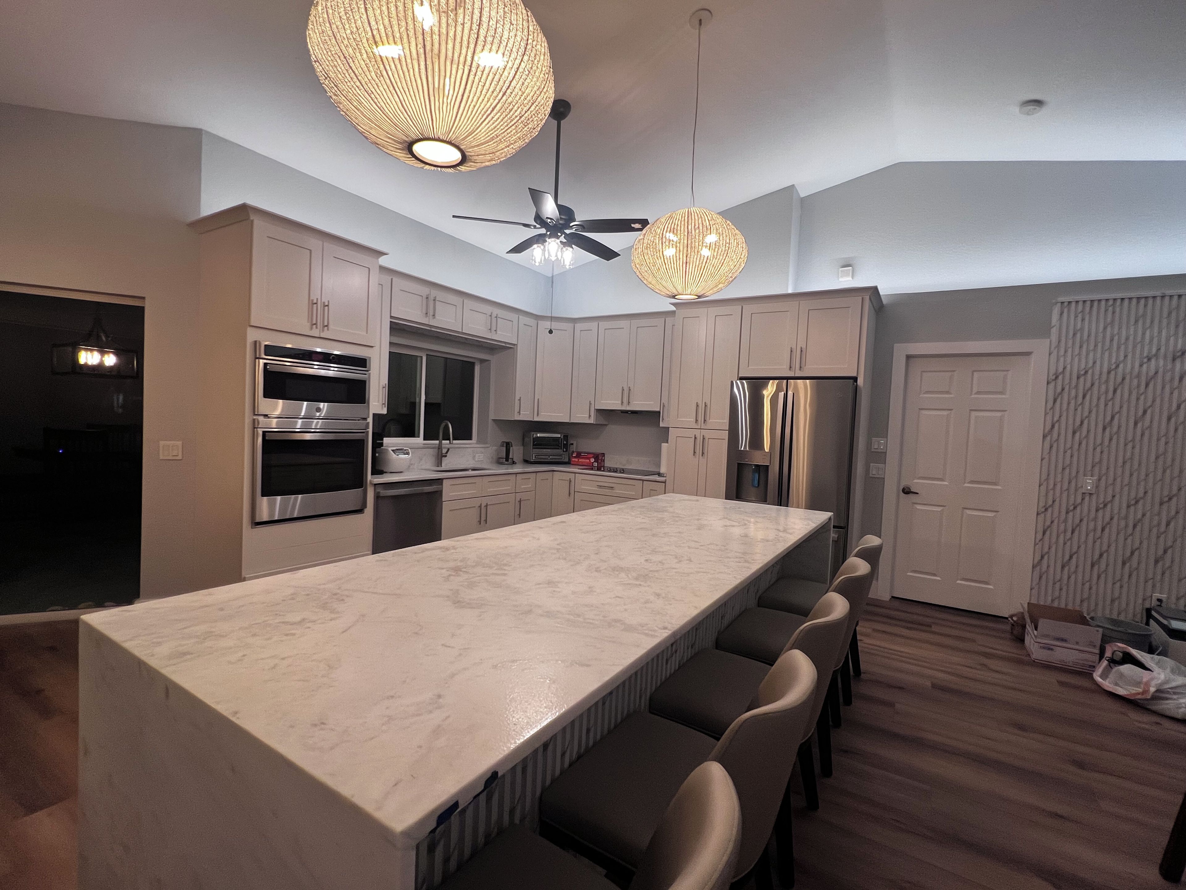 A modern kitchen with a large island, stainless steel appliances, and pendant lighting.