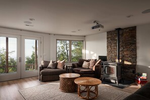 Ein modernes Wohnzimmer mit Kamin, zwei Sofas, einem runden Tisch und Blick durch große Fenster.