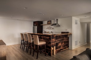 A modern kitchen with a wooden island, bar stools, a stainless steel refrigerator, and a built-in range hood. - Summit Shenandoah | Valley Views, Hot Tub, Sauna + Theater | 4BR, Sleeps 8 (Skyland Estates)