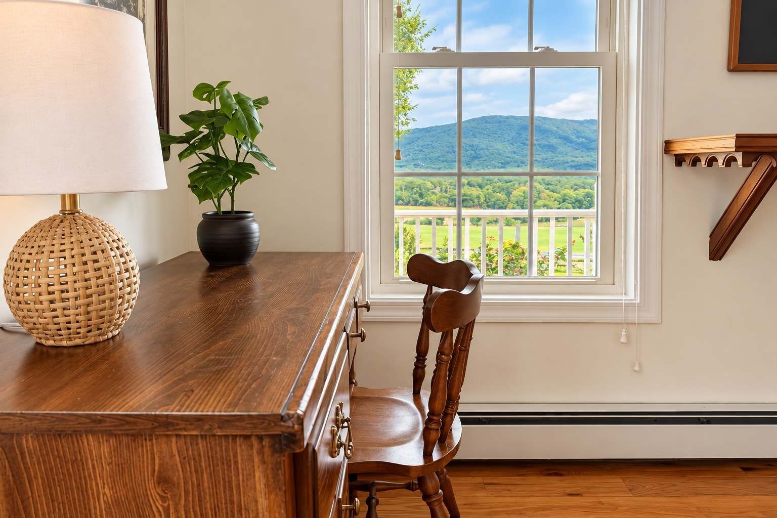 A wooden dining table with a lamp and a potted plant, a wooden chair, and a window with a view of a mountain.