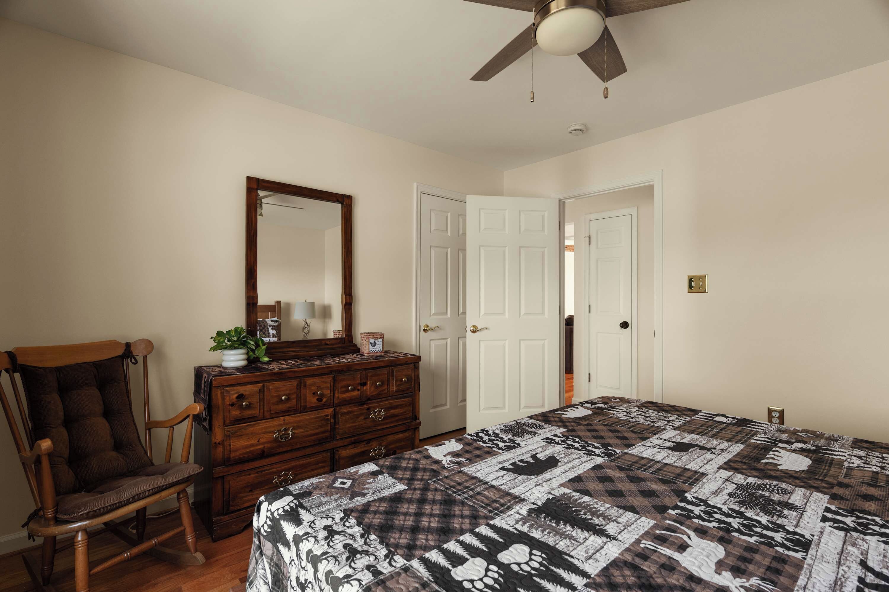 A bedroom with a bed, dresser, chair, and a ceiling fan.