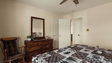 A bedroom with a bed, dresser, chair, and a ceiling fan.