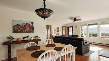 A dining area with a wooden table and chairs, a painting of a barn, and a ceiling fan.
