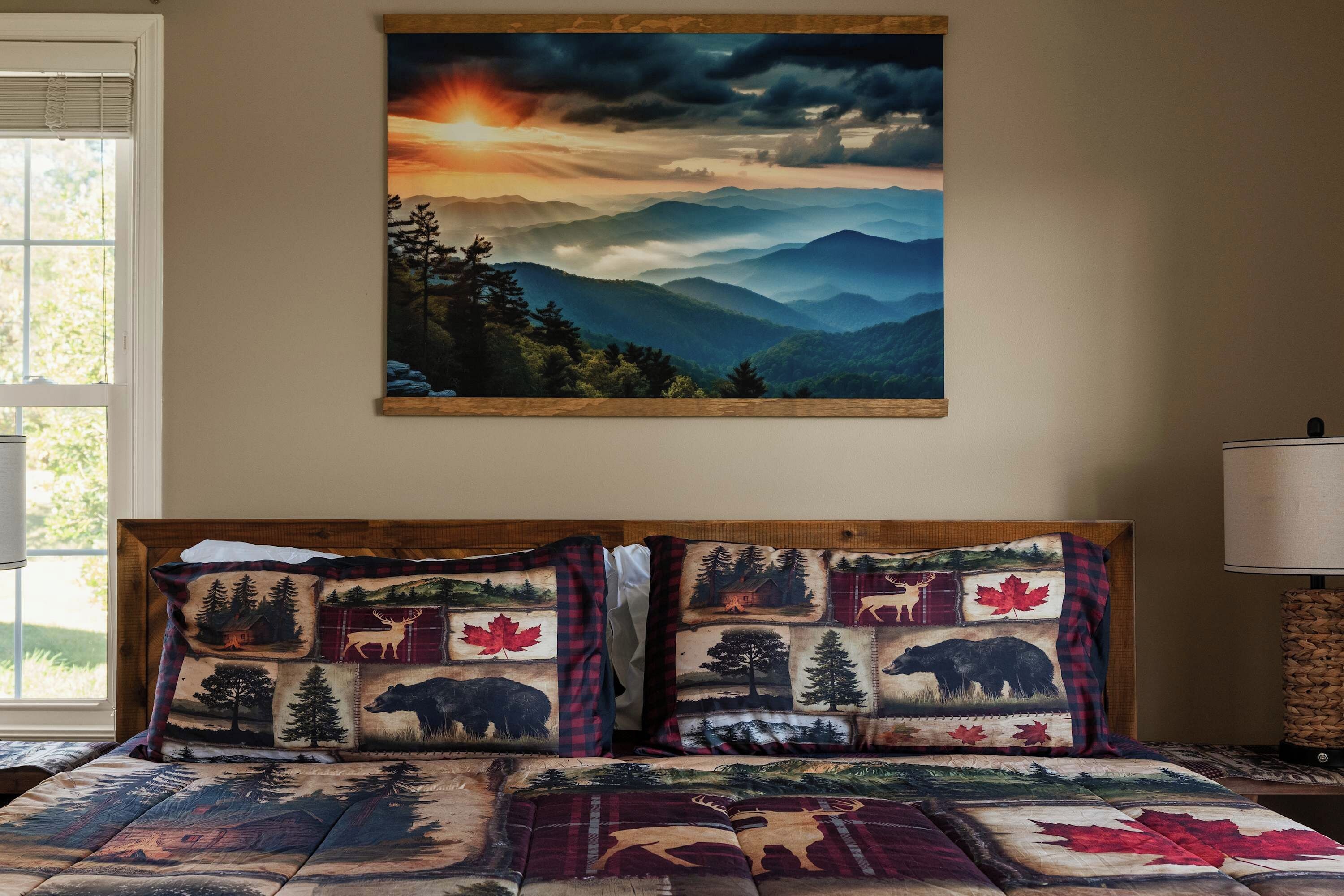 A bedroom with a large landscape painting on the wall, a bed with a quilted cover featuring animal prints, and a lamp on the side table.