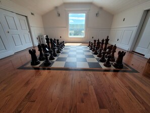 A room with a large chessboard set up on the floor, a door on the left, and a window on the right.
