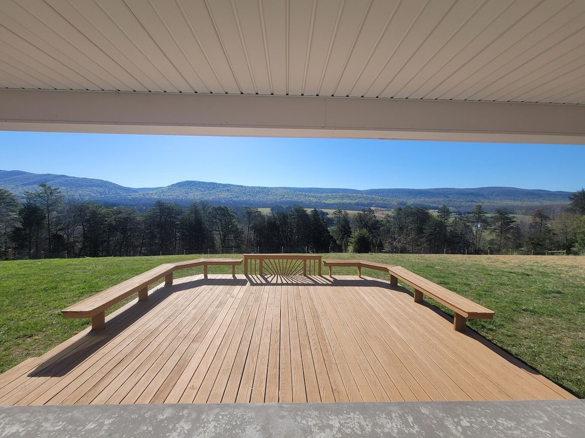 A wooden deck with benches and a railing, overlooking a grassy area and distant hills.
