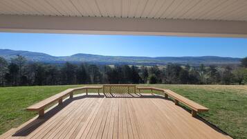A wooden deck with benches and a railing, overlooking a grassy area and distant hills.