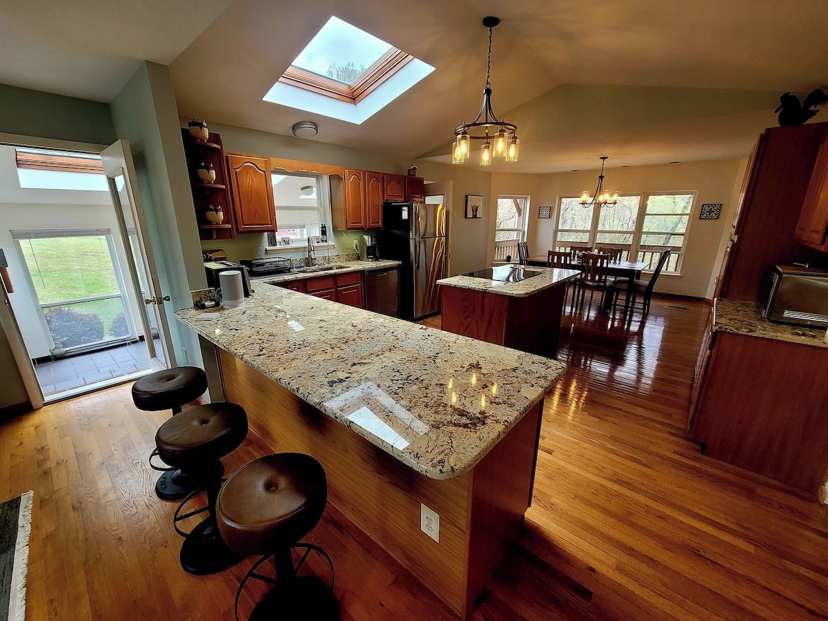 A kitchen with a central island, wooden cabinets, a skylight, and a dining area with chairs.