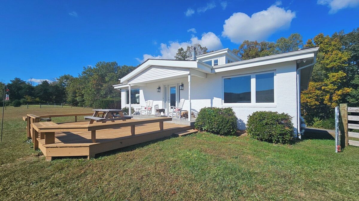 A single-story house with a covered patio area, a front porch with chairs, and a small deck.