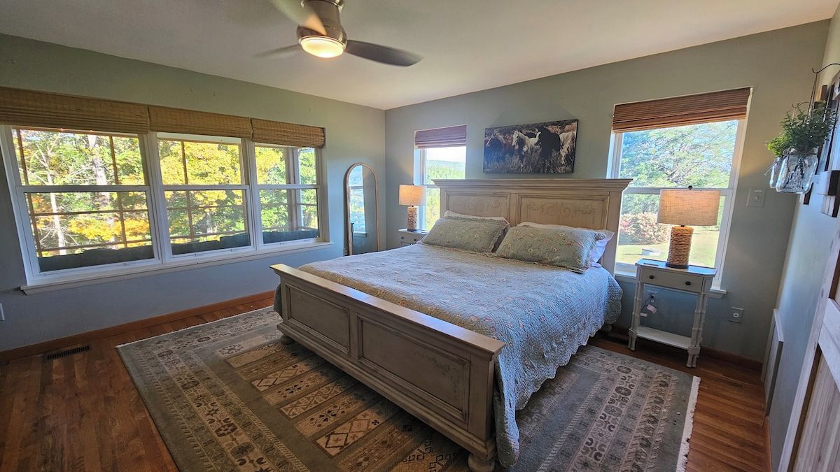 A bedroom with a large bed, two bedside tables, a ceiling fan, and multiple windows.