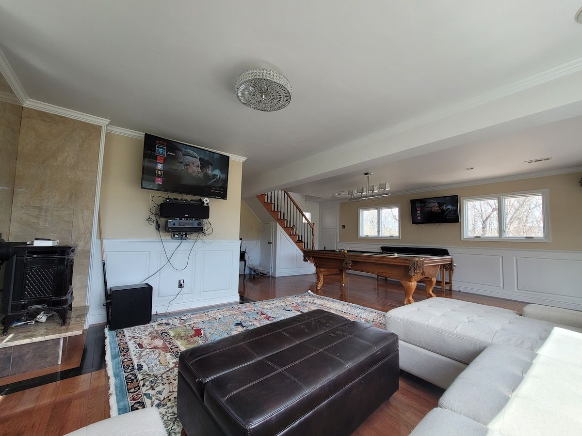Una sala de estar con chimenea, mesa de billar, sofá y televisor montado en la pared.