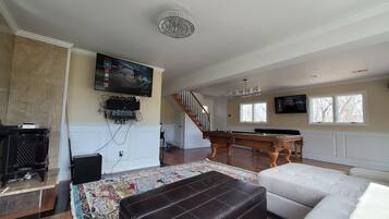 Una sala de estar con chimenea, mesa de billar, sofá y televisor montado en la pared.