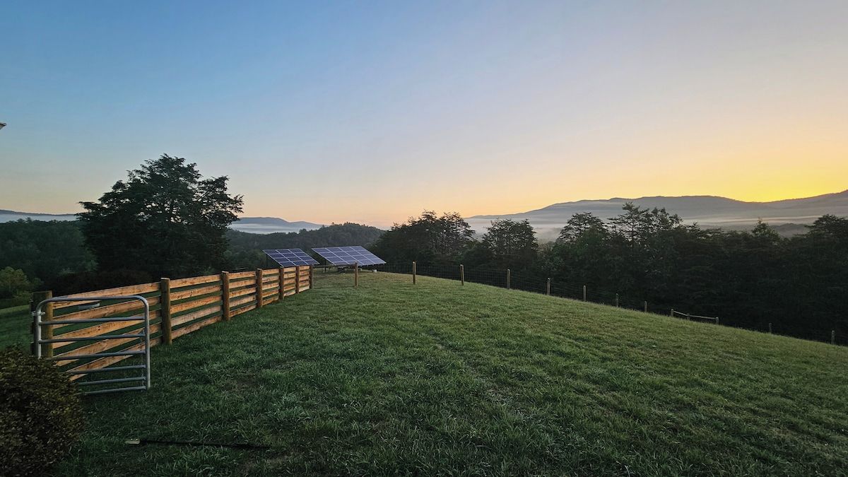 A grassy field with a wooden fence and solar panels.