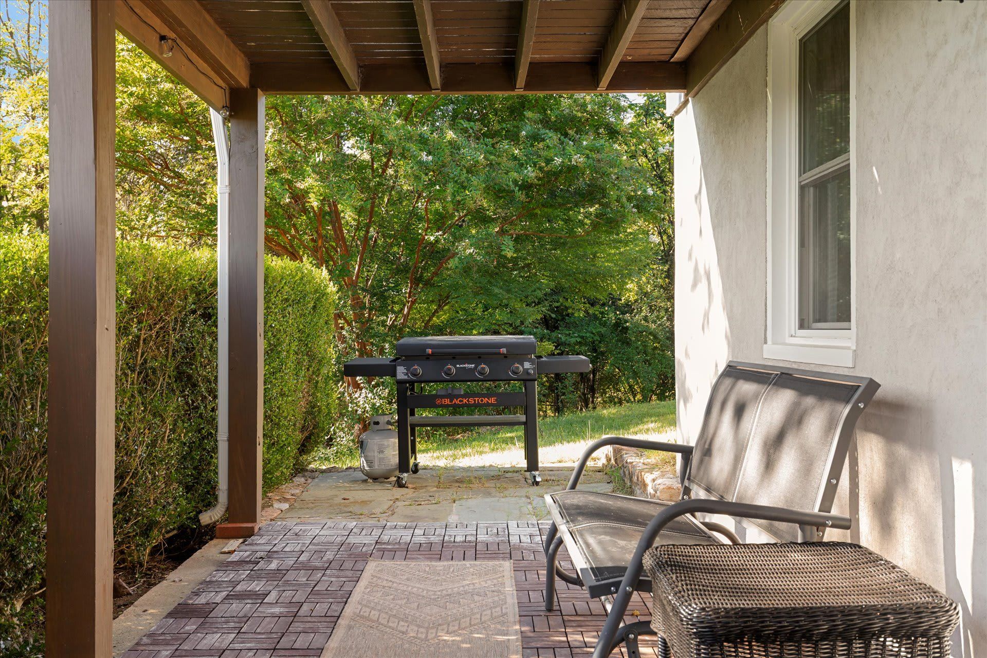 A covered patio with a grill, a bench, and a window.
