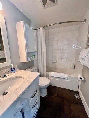 A bathroom with a sink, toilet, bathtub, and shower curtain. - Downtown Waterfront  | 2BR/2BA, Pool & Free Parking (Kelowna)