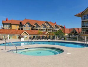 Een hotel met een zwembad, meerdere balkons en een dak met rode tegels.