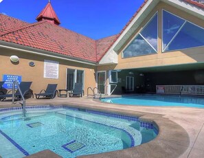 A swimming pool area with lounge chairs and a sign indicating hot tub availability. - Downtown Waterfront  | 2BR/2BA, Pool & Free Parking (Kelowna)