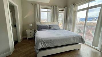 Ein Schlafzimmer mit einem Bett, Nachttischen und Blick auf die Stadt durch große Fenster.