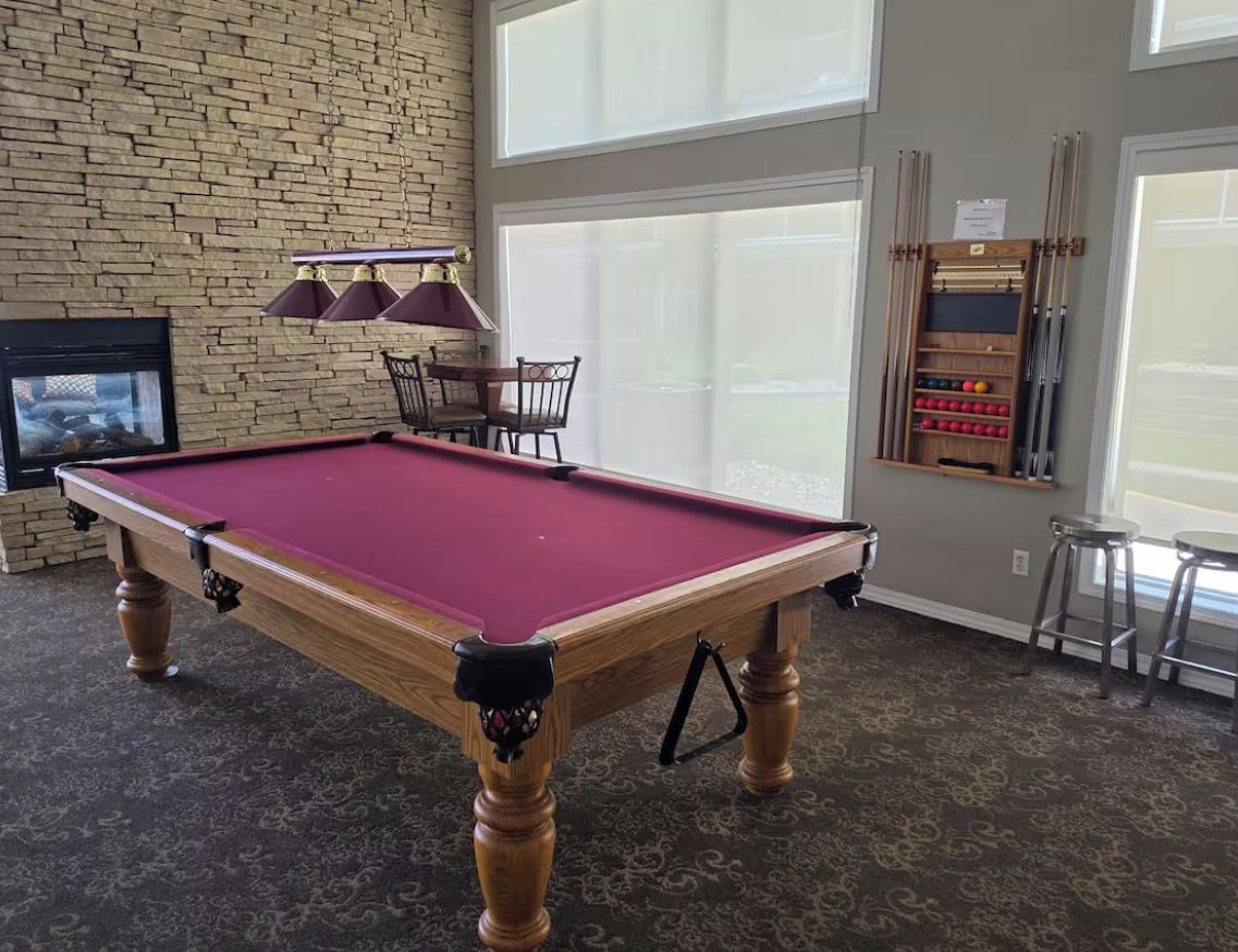 A pool table in a room with a brick wall, a fireplace, and a large window.