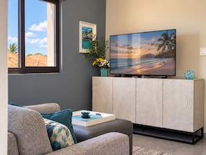 Ein Wohnzimmer mit einer Couch, einem Couchtisch, einem Schrank, einem Fernseher und einem Fenster mit Blick auf den Himmel und Gebäude.