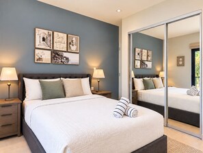 Ein Schlafzimmer mit einem großen Bett, Nachttischen, Lampen und einem Spiegel.
