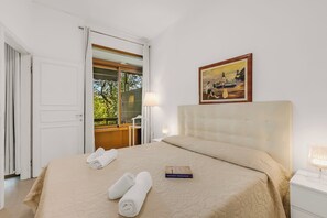 A hotel room with a bed, a painting, a window, and a door. - Park Apt With AC & Private Balcony, 300 mt to Sea, Torre del Lago, Italy (Torre del Lago)