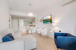 A modern living room with a sofa, a blue armchair, a dining area with a table and chairs, a kitchen in the background, and a large TV mounted on the wall. - Park Apt With AC & Private Balcony, 300 mt to Sea, Torre del Lago, Italy (Torre del Lago)