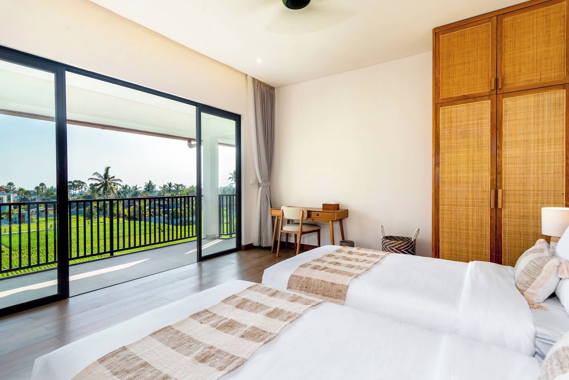 Habitación de hotel con balcón amplio, cama con ropa blanca, armario de madera y escritorio con silla.