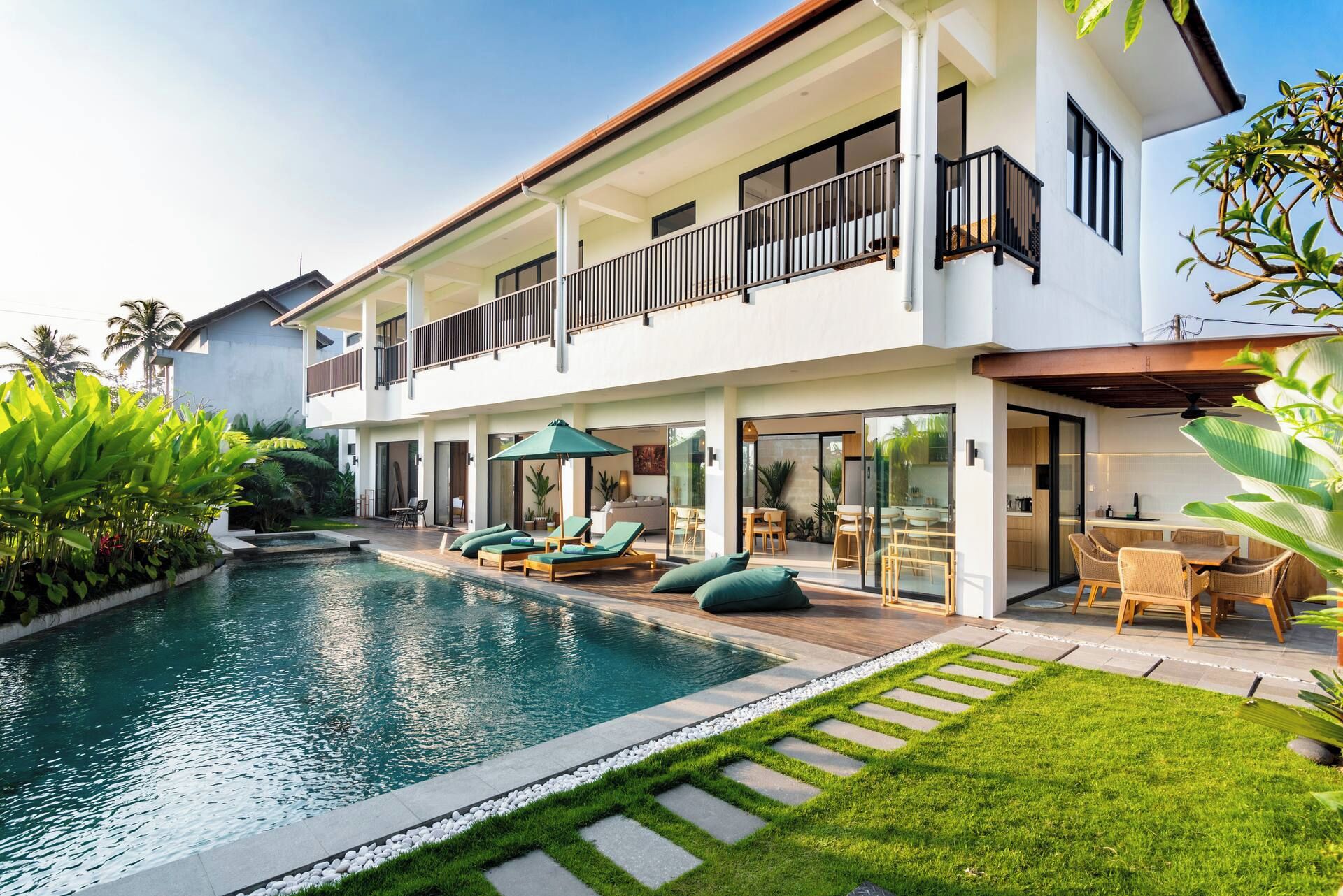 Una casa de dos pisos con piscina, mobiliario exterior y balcón.