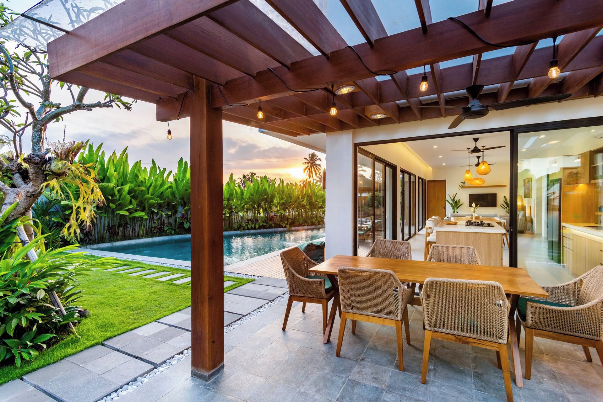 A covered outdoor dining area with a pool, wicker furniture, and a view of the kitchen.