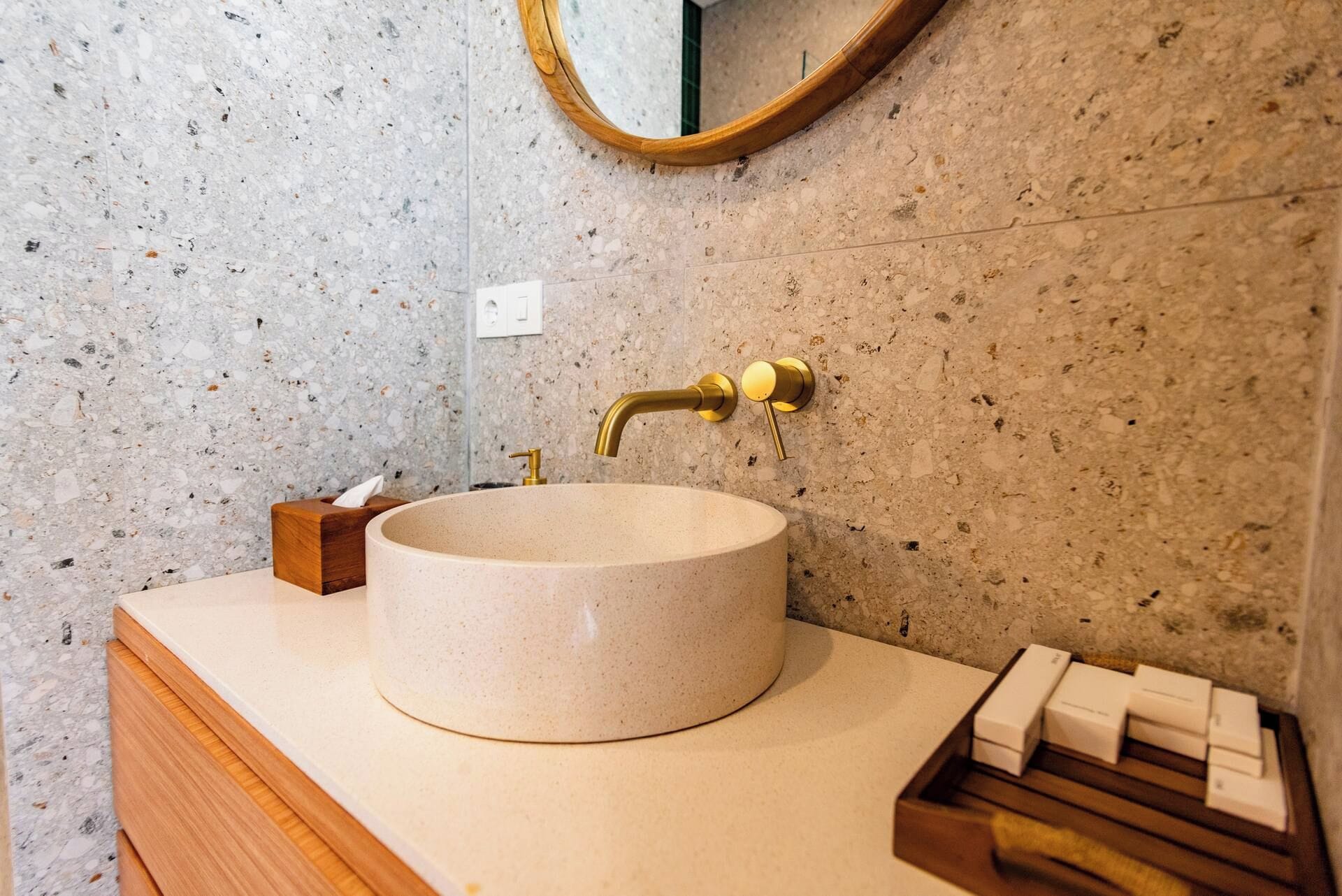 Un baño con un lavabo redondo, un mueble de tocador de madera, un espejo y un perchero para toallas.