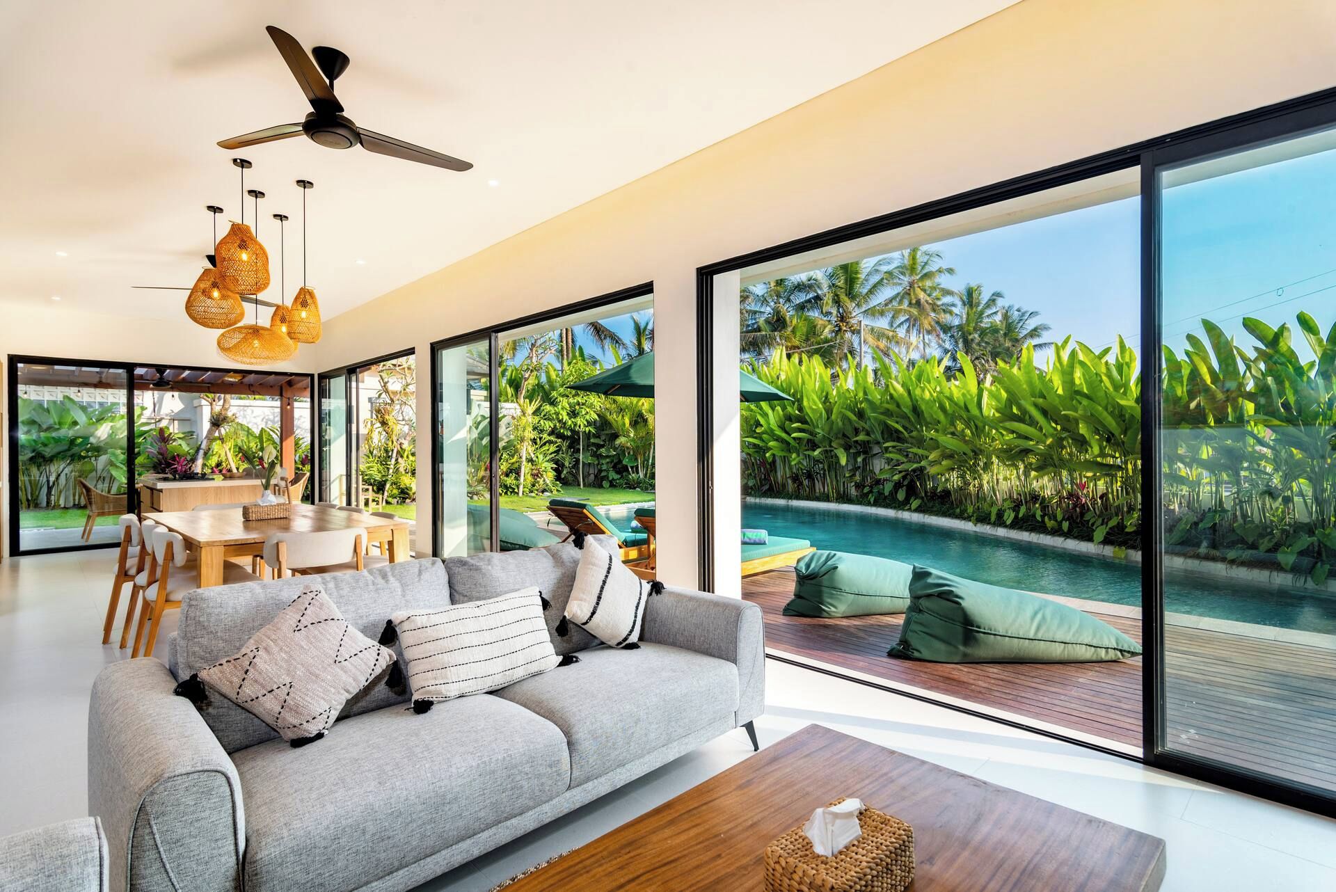 Una sala de estar moderna con sofá, una mesita de centro y vistas a una piscina y jardín tropical.