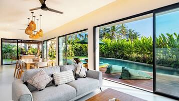 Una sala de estar moderna con sofá, una mesita de centro y vistas a una piscina y jardín tropical.