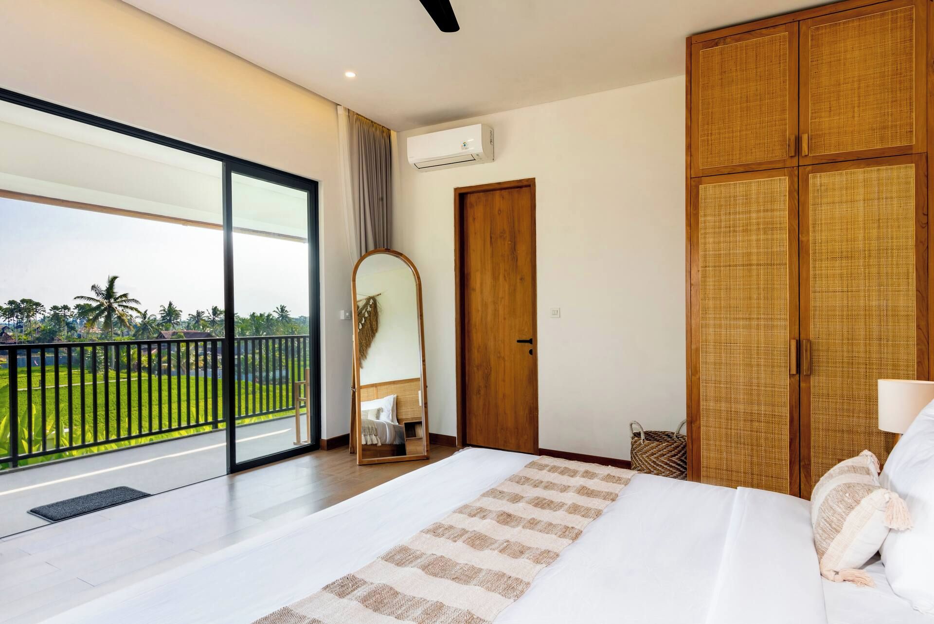 Habitación de hotel con una cama grande, un armario, un espejo y un balcón con vistas a zonas verdes.