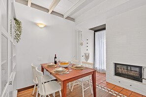 A dining area with a wooden table set for four, white chairs, a fireplace, and a hanging plant. - Borgo Della Motta Swimming Pool &Golf, Travedona Monate, Italy (Travedona Monate)