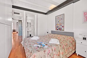 A bedroom with a bed, a bedside table, a nightstand, a wall-mounted artwork, and a bathroom visible through an open door. - Borgo Della Motta Swimming Pool &Golf, Travedona Monate, Italy (Travedona Monate)