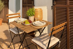 An outdoor dining area with a wooden table, two cushioned chairs, a potted plant, a woven basket, and a glass of water. - Sanary Apt N2, Sanary-sur-Mer, France (Sanary-sur-Mer)
