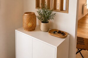 Un mueble blanco con una lámpara tejida, una planta en maceta y una bandeja de madera con llaves y gafas de sol.