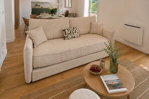 A living room with a beige sofa, a coffee table with a magazine, a bowl of fruit, and a green vase. - Sanary Apt N1, Sanary-sur-Mer, France (Sanary-sur-Mer)