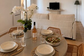 Un coin repas avec une table ronde dressée pour quatre personnes, des assiettes blanches, des verres à vin et un saladier rempli de salade.
