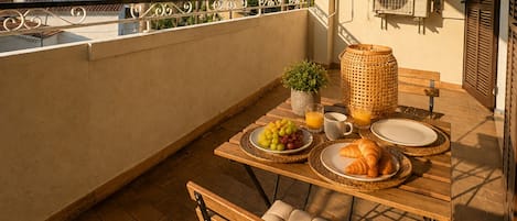 A breakfast setup on a balcony with a table, chairs, and a view of palm trees and buildings.