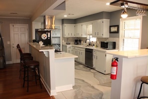 A kitchen with white cabinets, a central island, bar stools, a microwave, and a fire extinguisher. - Spacious 4-bedroom house in fantastic Columbus with AC and gym access (Columbus)