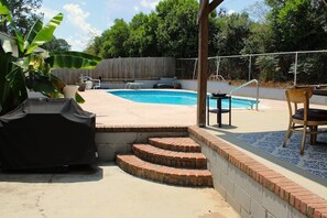 A backyard with a swimming pool, a covered grill, and a patio area with a table and chairs. - Spacious 4-bedroom house in fantastic Columbus with AC and gym access (Columbus)