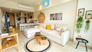 A modern living room with a sofa, coffee table, and a dining area with stools. - Jacana Sunset 205 | Bucerias Beach & Rooftop Infinity Pool (Bucerias)