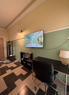 Una habitación con una televisión instalada en la pared, una silla de oficina negra, un escritorio con una lámpara y un suelo a cuadros.