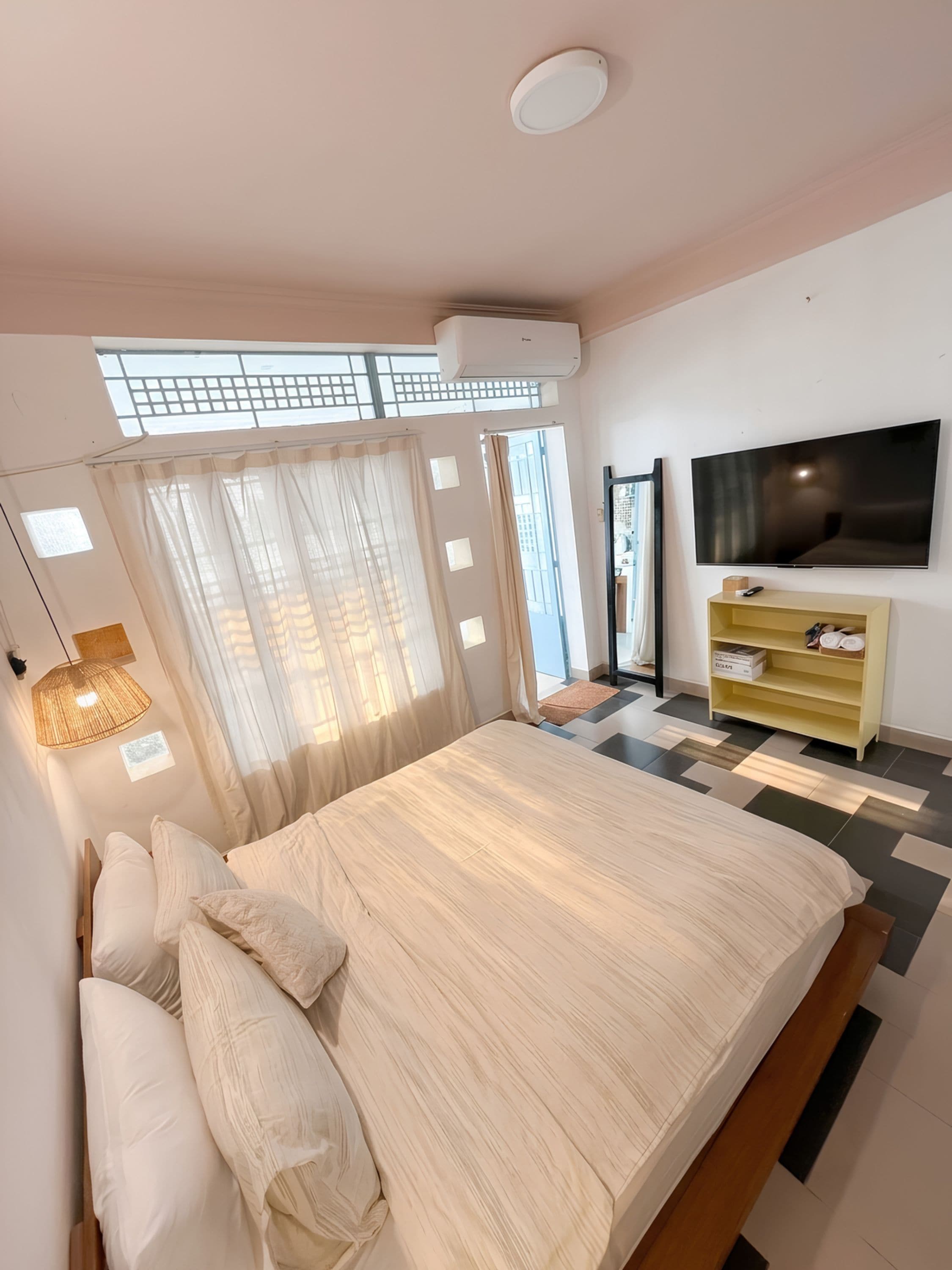 A bedroom with a bed, a TV, a shelf, and a window with curtains.