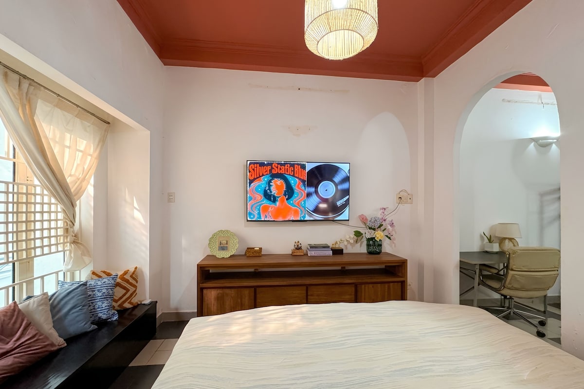 Un dormitorio con una cama grande, un televisor montado en la pared, una mesita consola de madera y un escritorio con una silla.