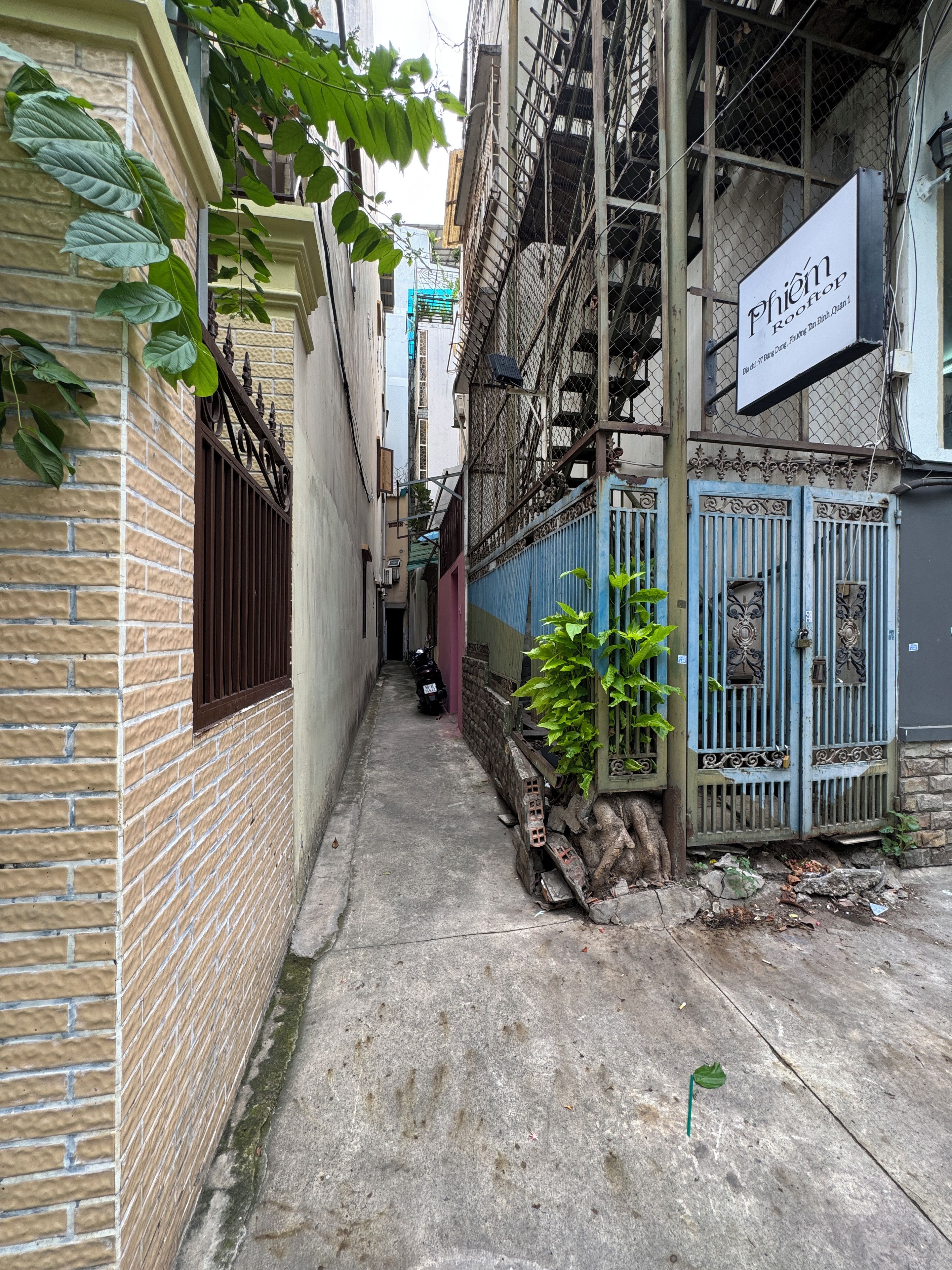 Un callejón estrecho con paredes de ladrillo, una reja metálica y una moto estacionada al costado.