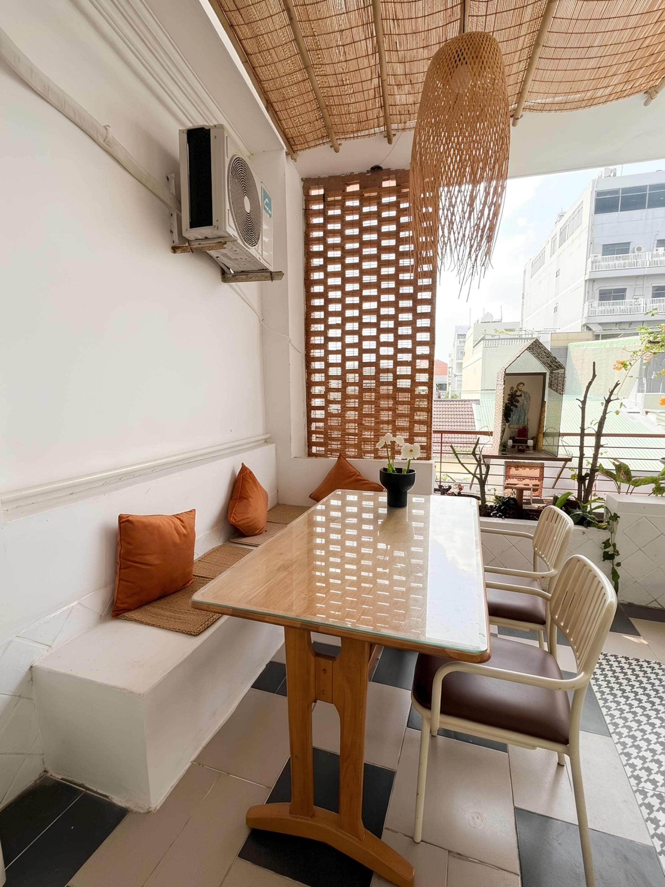 A dining area with a glass table, wooden chairs, a woven ceiling, and a view of buildings.
