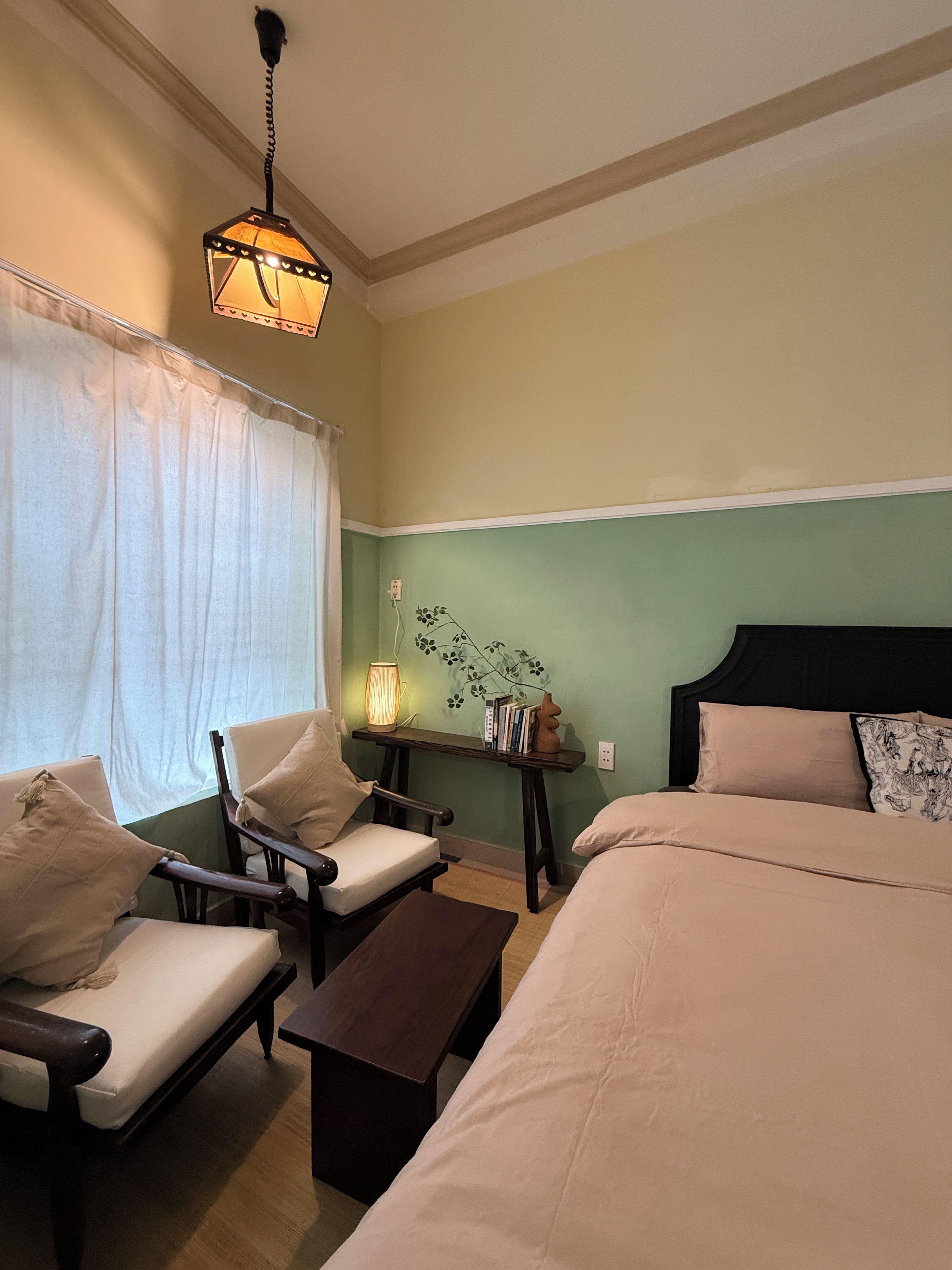 Un dormitorio con una cama, dos sillas, una mesita de noche, una lámpara y un estante en la pared.